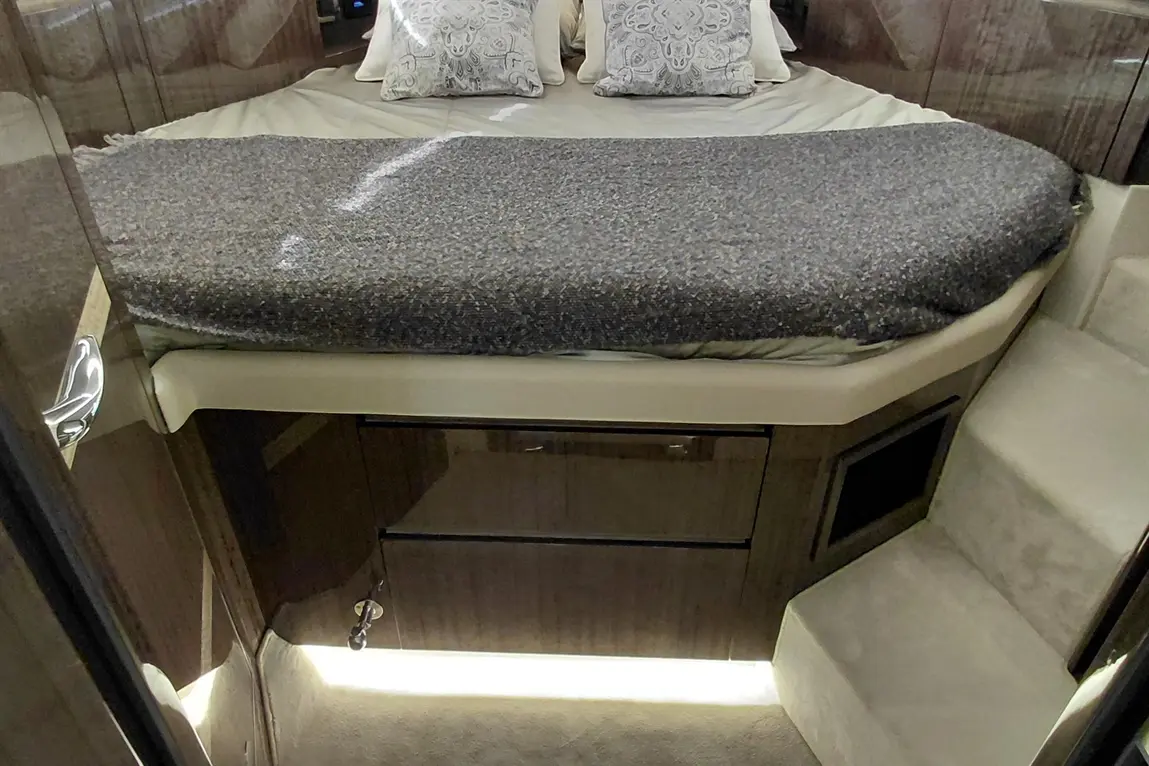 Luxurious boat interior featuring a plush bed with decorative pillows, drawer storage below, and softly illuminated steps.